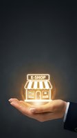Close-up of hand holding glowing neon e-shop storefront icon against dark background. Represents online retail, digital commerce, and business growth for web and marketing use.
