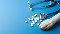 Medical stethoscope with white pills and dog paw on blue background for veterinary healthcare and pet medicine concepts.