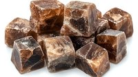 Rough chunks of dark brown chocolate scattered on white background, raw cacao pieces with uneven surfaces showing natural crystalline structure and texture.