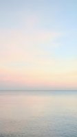 Serene ocean horizon at dawn with soft pastel sky transitioning from pink to blue, calm water reflecting gentle light. Suitable for wellness, travel, and meditation backgrounds.