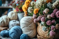 Cozy knitting composition with soft yarn balls in beige and blue shades next to woven basket with colorful dried flowers, creating warm crafting atmosphere.
