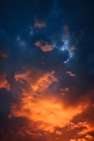 Dramatic sunset sky with glowing orange clouds against deep blue atmosphere, scattered stars visible through breaks in cloud coverage, creating ethereal mood.