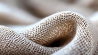 Natural linen fabric close up macro shot showing textile weave pattern and texture in beige and white tones for background design.