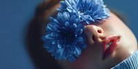 Young woman with blue chrysanthemum flowers covering eye in artistic portrait with dramatic lighting and shadows on blue background for beauty concepts.