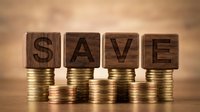 Wooden letter blocks spelling SAVE on stacks of golden coins against warm background representing financial savings and money management concepts.