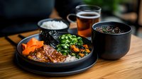 Asian braised beef bowl with steamed rice, carrots and green onions served with hot tea and miso soup on wooden table, restaurant setting.
