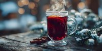 Steaming glass of mulled wine with spices on rustic wooden table decorated with fir branches, creating cozy winter atmosphere.