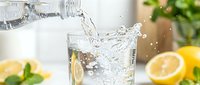 Fresh water pouring into glass with lemon slices and mint leaves on kitchen counter. Healthy hydration lifestyle concept for wellness and detox drinks.