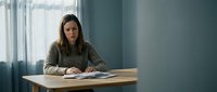 Young professional woman sitting at wooden desk in modern office interior working with documents and papers during daytime near window.