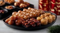Asian cuisine platter featuring glazed chicken wings, grilled meat skewers and dumplings served on black plate with traditional red and gold decorations.