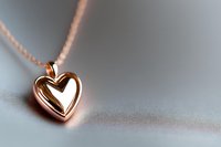 Rose gold heart pendant necklace on delicate chain against soft gray background, romantic jewelry macro photography with selective focus and copy space.