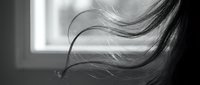 Young woman with flowing hair in motion by window, black and white portrait capturing movement and natural light for artistic photography projects.