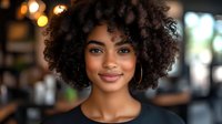 Young woman with natural curly afro hairstyle smiling at camera in soft focus cafe setting. Professional portrait with warm bokeh background.
