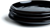 Stack of elegant black ceramic plates with glossy finish on white background, close-up view showing modern minimalist tableware design and texture.