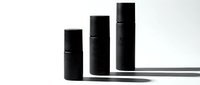Three black cosmetic spray bottles in ascending height arrangement casting shadows on white background for skincare and beauty product mockups.