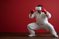 Young Caucasian man in white tracksuit wearing VR headset and red boxing gloves practicing virtual reality fitness training on red background.