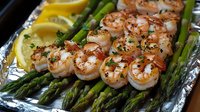 Grilled shrimp skewers served on fresh asparagus spears with lemon wedges and herbs on aluminum foil, showcasing succulent seafood and vibrant vegetables.