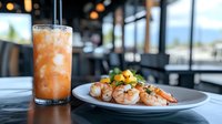 Grilled shrimp with mango salsa served on white plate alongside tropical cocktail with crushed ice, restaurant setting with ocean view background.