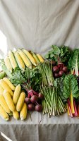 Fresh seasonal vegetables including corn, asparagus, beets and leafy greens arranged on neutral linen fabric for healthy cooking and farm-to-table cuisine.
