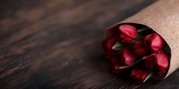 Fresh red tulip bouquet wrapped in craft paper lying on dark wooden surface, romantic floral composition with soft natural lighting and copy space.