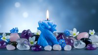 Blue dragon candle burning among colorful gemstones and crystals creating mystical atmosphere for meditation, spirituality and wellness practices.