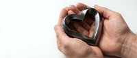 Male hands gently holding heart-shaped chocolate mold on white background. Baking, cooking preparation concept for Valentine's Day treats.