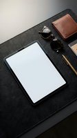 Modern workspace with blank tablet screen, leather wallet, sunglasses and pen on dark felt desk mat for business mockup and branding presentations.