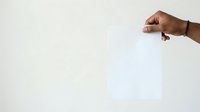 Male hand with dark skin tone holding blank white paper sheet against neutral background for mockup and branding purposes.