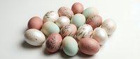 Collection of naturally dyed Easter eggs in soft pastel colors including pink, green, cream and speckled brown arranged on white background for spring decor.