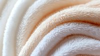 Soft white plush fabric texture in gentle folds and waves creates luxurious background pattern with delicate shadows and highlights. Suitable for textile and comfort concepts.