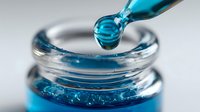 Turquoise liquid drops from glass dropper into transparent container creating ripple effect on surface against light gray background.