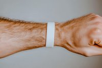 Male hairy arm wearing blank white paper wristband against neutral background. Mock-up for event access, festival, hospital or club identification.
