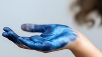 Open palm of Caucasian woman's hand covered in vibrant blue paint, suggesting creativity, artistic expression, and transformation.