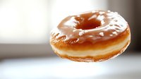 Glazed donut floating in air against blurred background, showcasing sweet vanilla frosting and soft dough texture in natural lighting. Appetizing bakery photography.