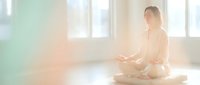 Young Asian woman practicing meditation in lotus position on yoga mat in bright sunlit room with peaceful atmosphere for wellness and mindfulness.