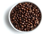Fresh roasted coffee beans in round white ceramic bowl against white background, overhead view showing rich brown color and natural texture of arabica beans.