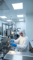Scientist in protective suit working with pharmaceutical equipment in sterile cleanroom laboratory for drug manufacturing and quality control testing.