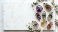 Healing crystals and gemstones arranged on white marble surface with eucalyptus leaves for spiritual wellness meditation and energy cleansing practices.