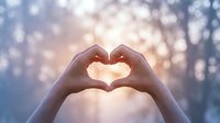 Hands forming heart shape against soft bokeh background with warm sunlight creating romantic atmosphere for love and affection concepts.