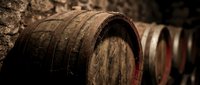 Aged wooden barrels stacked in a cellar or winery, showing weathered oak construction and metal bands, used for aging wine, whiskey, or spirits.