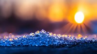 Glowing winter sunrise over crystalline snow and ice formations creating magical bokeh effect with sunburst and golden morning light on frozen surface.