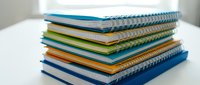 Stack of colorful spiral-bound notebooks and composition books arranged on white surface for back to school office supplies and educational materials.