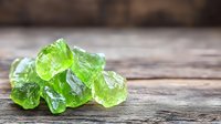 Raw green peridot crystals on rustic wooden background with selective focus, natural mineral gemstones displaying translucent crystalline structure.