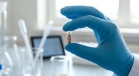 Medical researcher in blue latex gloves examining microchip or electronic component in modern laboratory setting with scientific equipment and test tubes.
