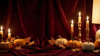 Autumn harvest display with orange and white pumpkins, burning candles in brass holders against rich burgundy velvet drapes for seasonal home decor.