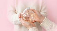 Woman hands holding crystal glass globe on soft pink background representing global care, environmental protection and world conservation concept.