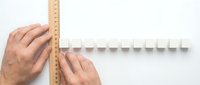Hands measuring white plastic wall-mounted coat rack with wooden ruler on light background for home organization and interior design projects.