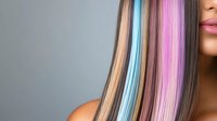 Young woman with vibrant rainbow colored hair extensions featuring pink blue and blonde streaks on gray background for beauty salon concepts.