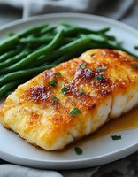 Pan-seared cod fillet with golden-brown crust, fresh green beans, and chive garnish on white plate. Ideal for food blogs, recipe websites, and culinary publications.