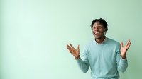 Excited young man with dark hair and medium brown skin tone wearing light blue sweater gesturing with open palms against mint green background, expressing enthusiasm and joy for advertising and marketing campaigns.